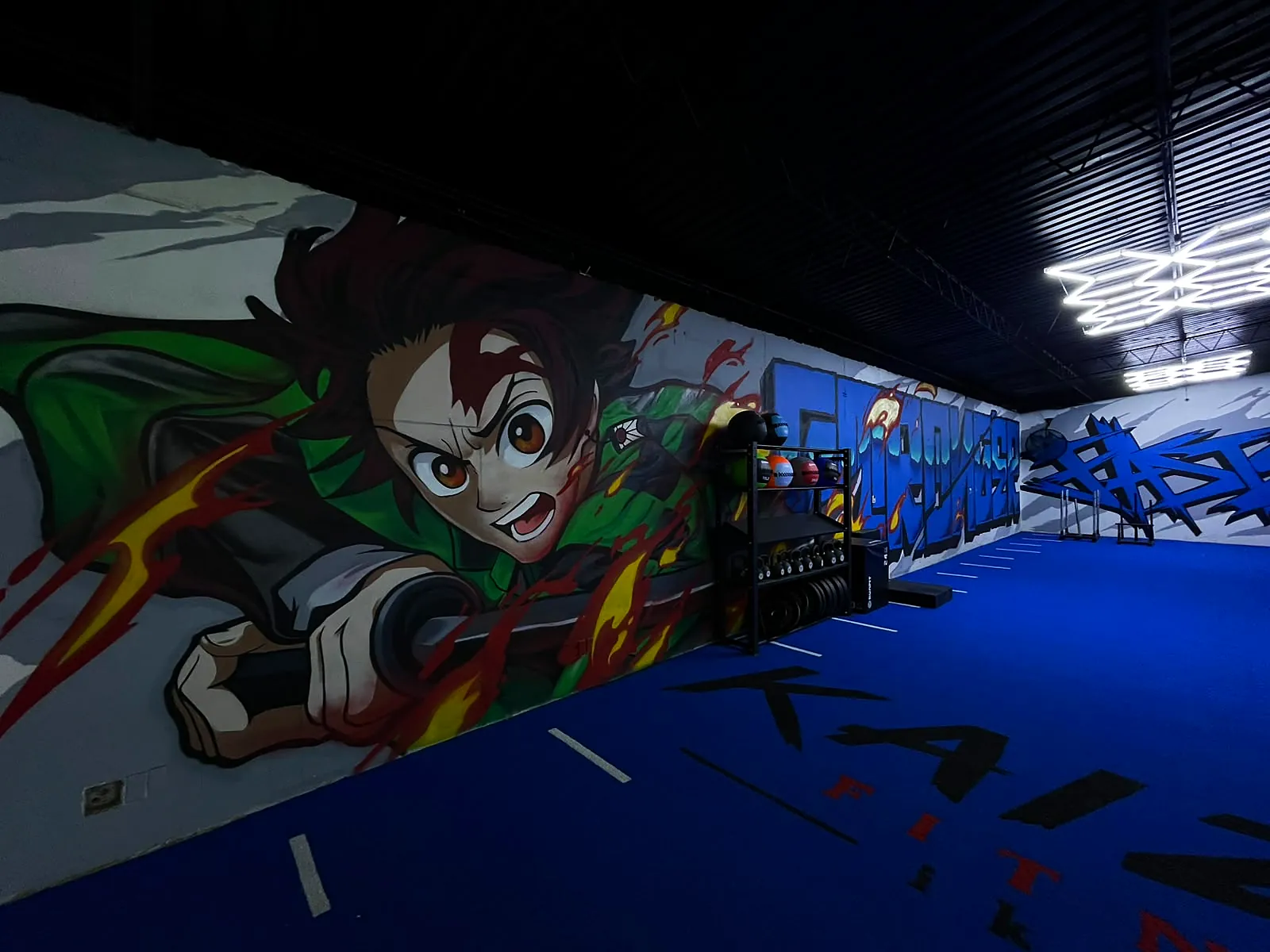 Zona HYROX: pasto azul con carriles y el mural de Tanjiro