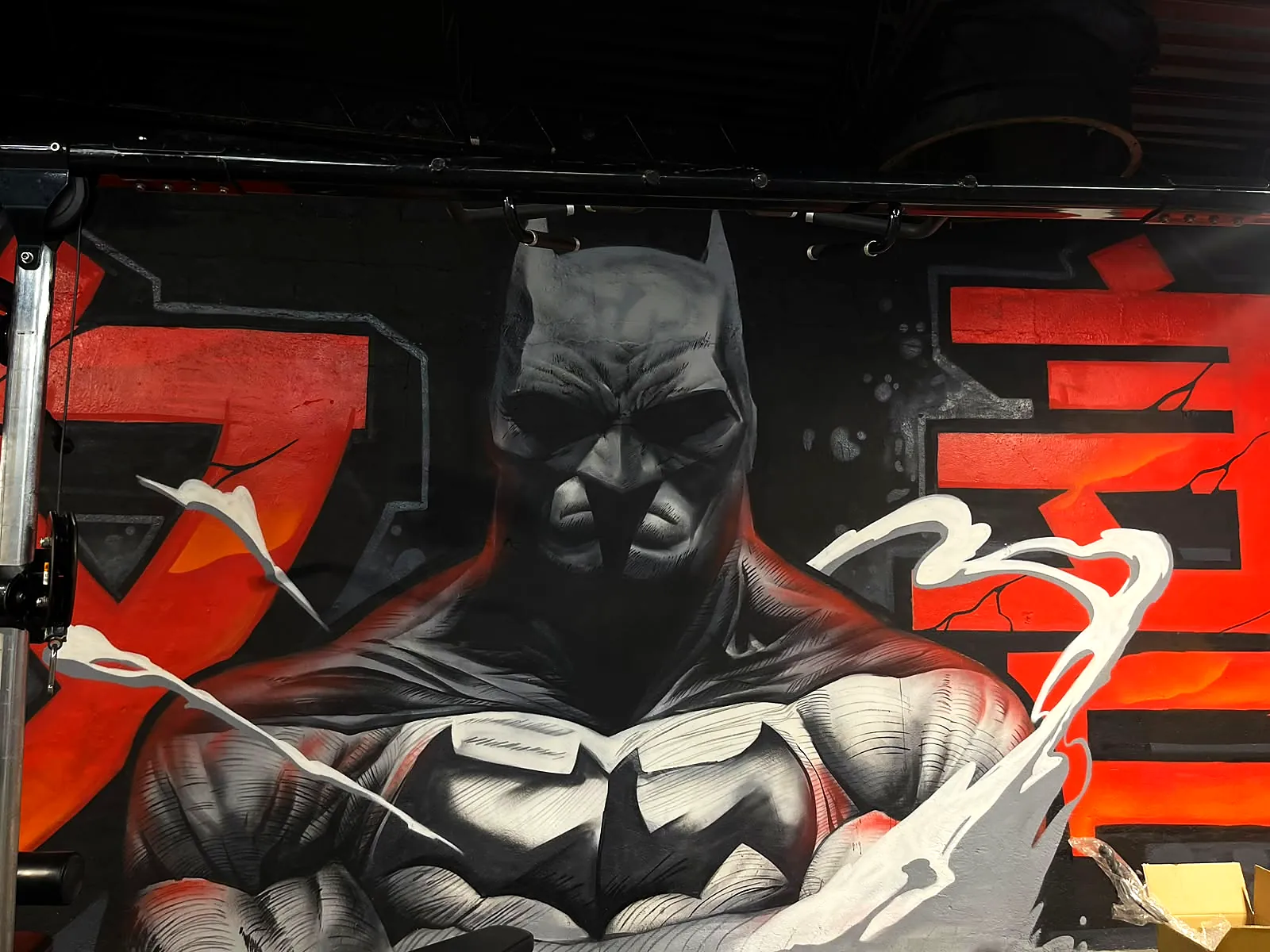 Mural de Batman pintado a mano sobre un muro rojo y negro
