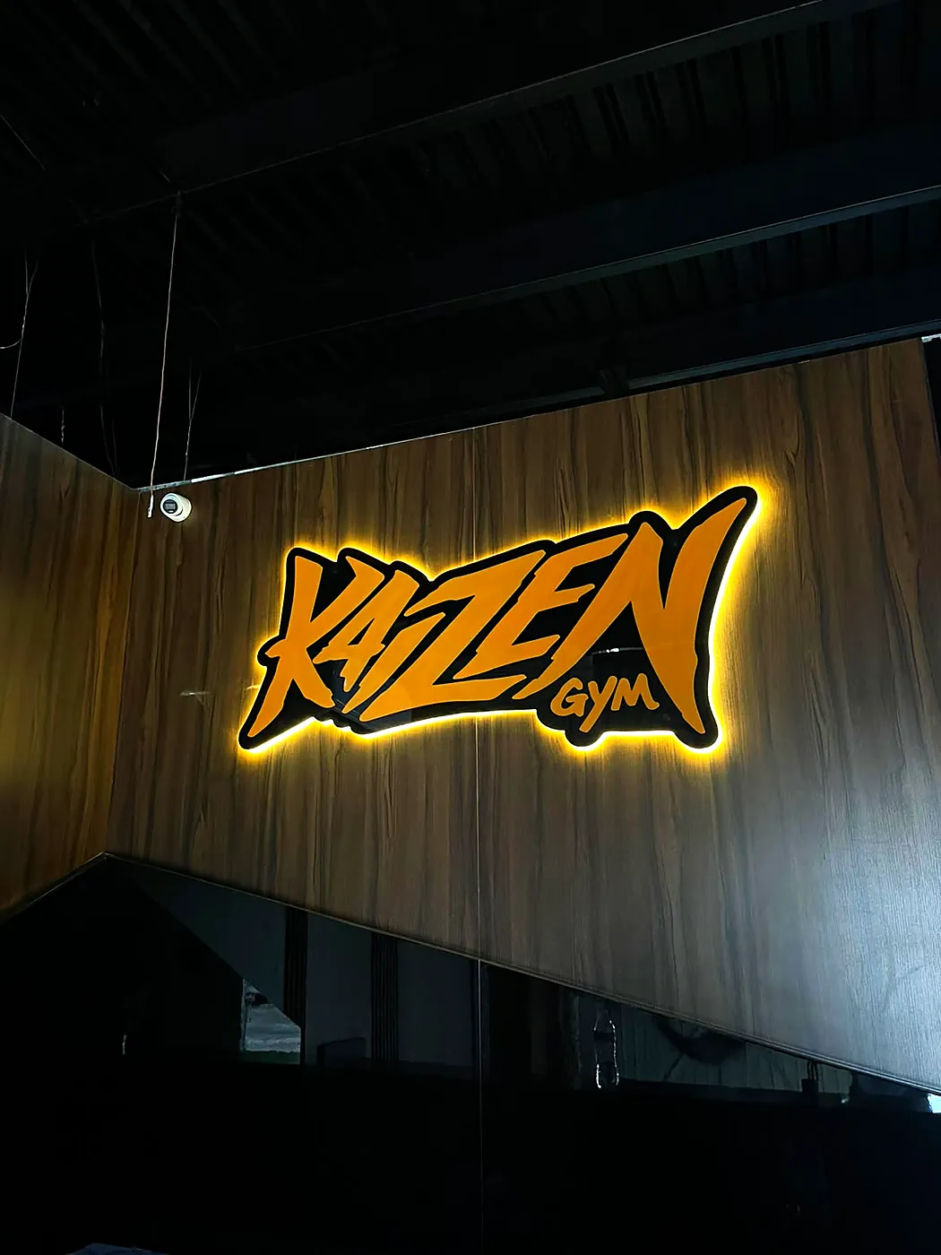 Recepción de Kaizen Gym: muro de madera con el letrero naranja retroiluminado